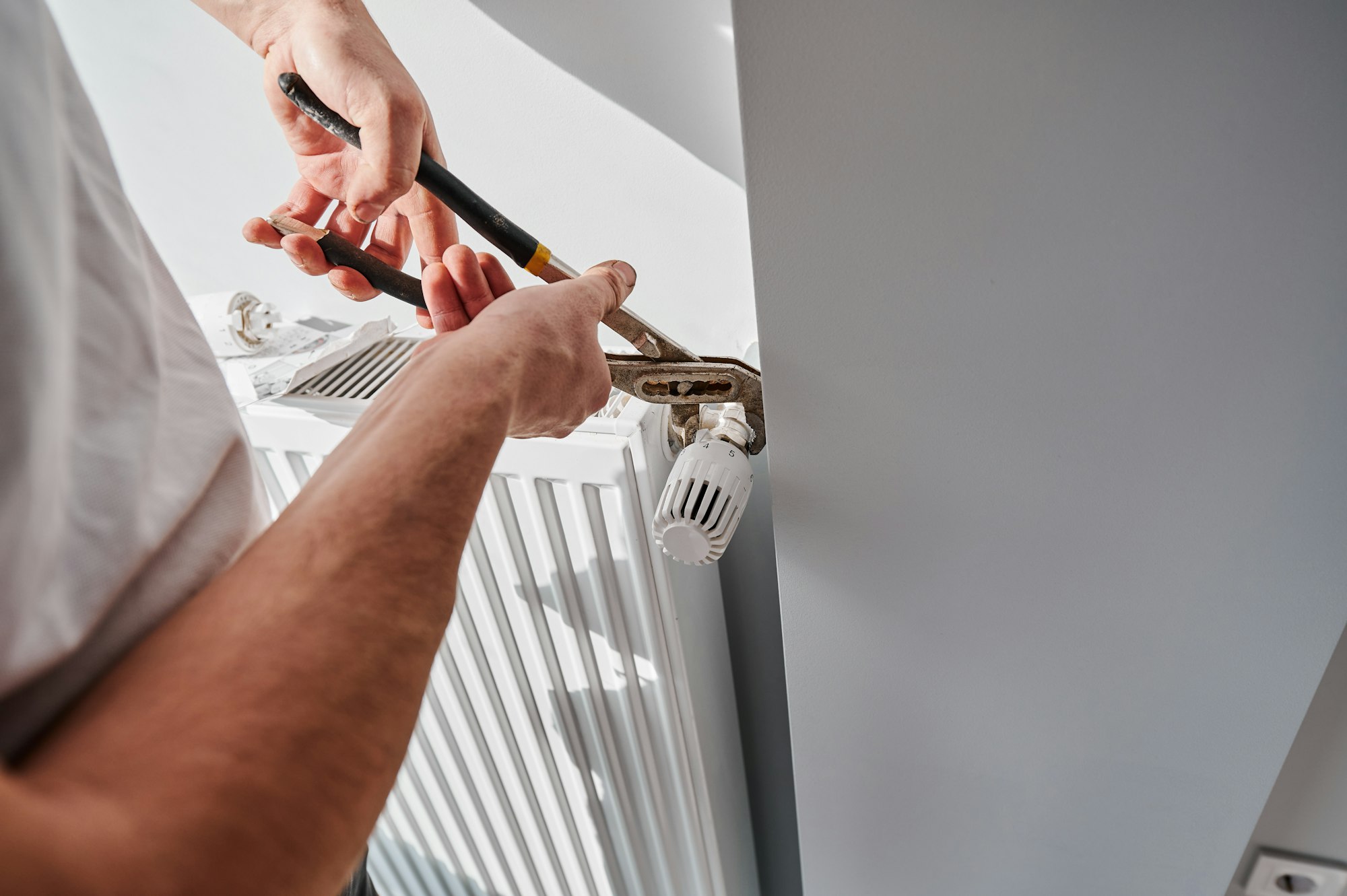 Male worker hands installing heating radiator in apartment.